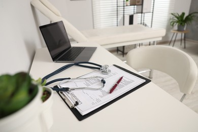 Photo of Clipboard, stethoscope, laptop and pen on white table in clinic. Doctor's workplace