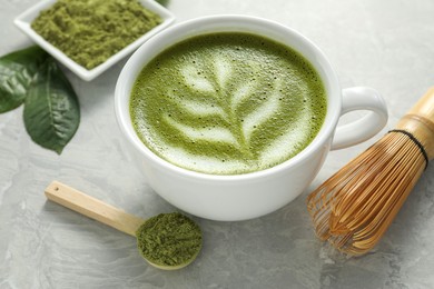 Cup of fresh matcha latte, powder and bamboo whisk on grey marble table, closeup