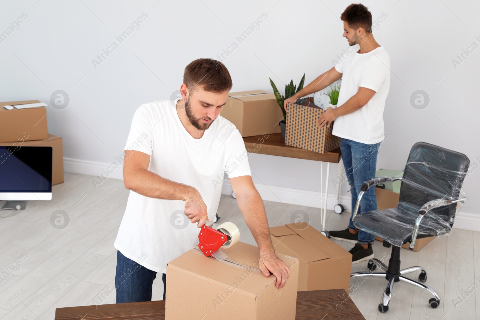 Photo of Young worker packing box and his colleague in office. Moving service