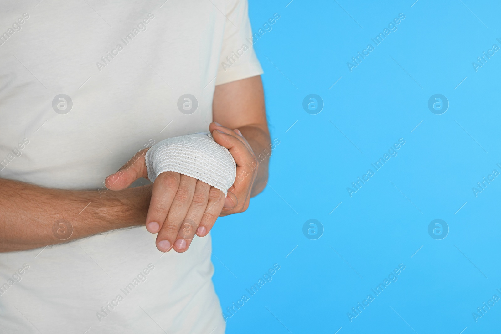 Photo of Man with hand wrapped in medical bandage on light blue background, closeup. Space for text