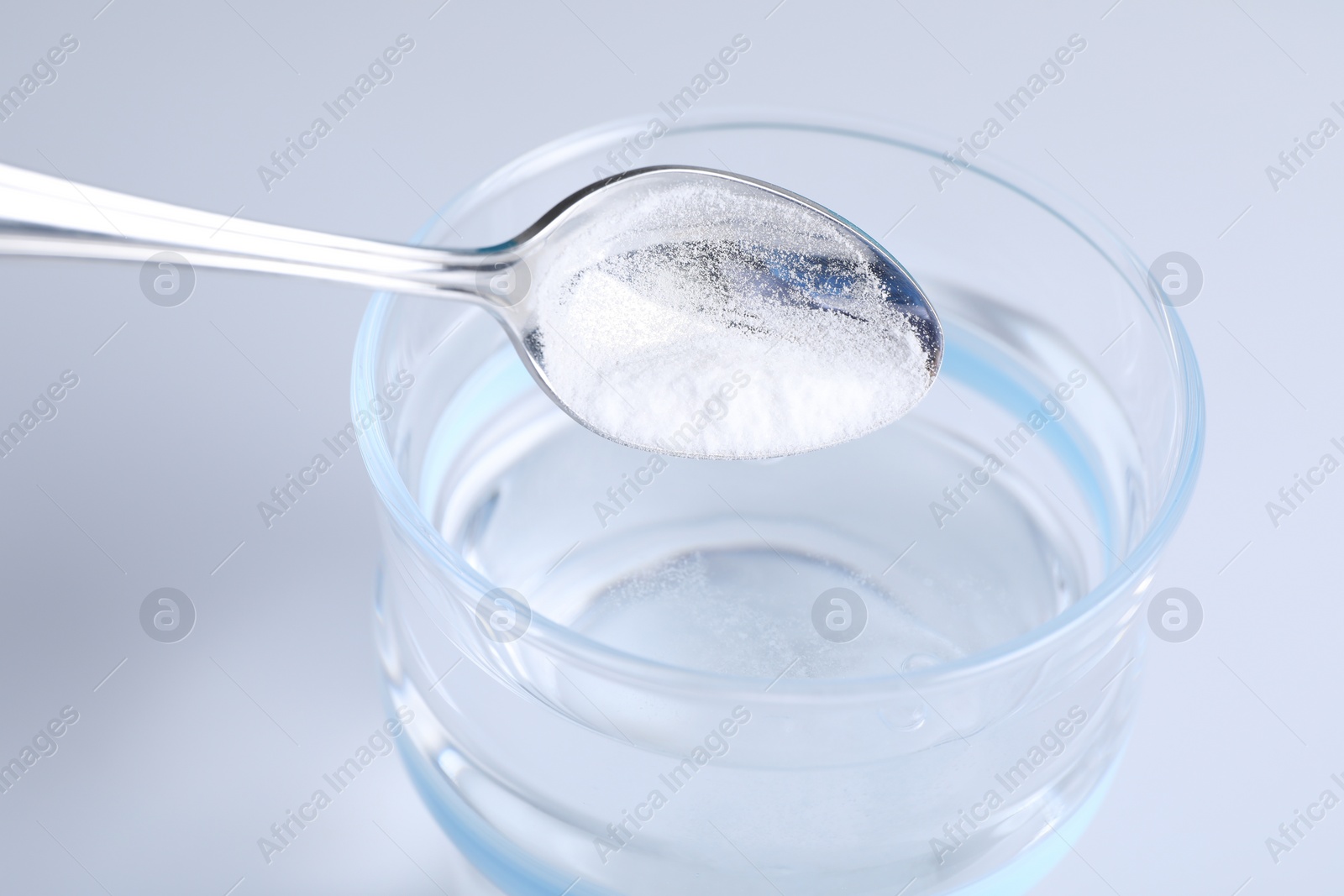 Photo of Adding baking soda into glass of water on light background, closeup