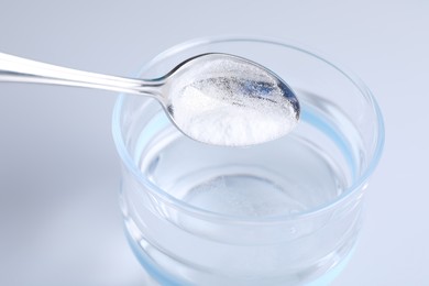 Photo of Adding baking soda into glass of water on light background, closeup