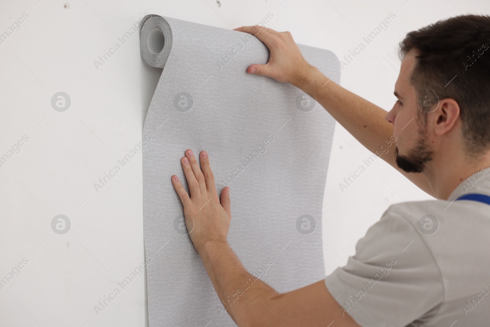 Photo of Man hanging stylish gray wallpaper in room