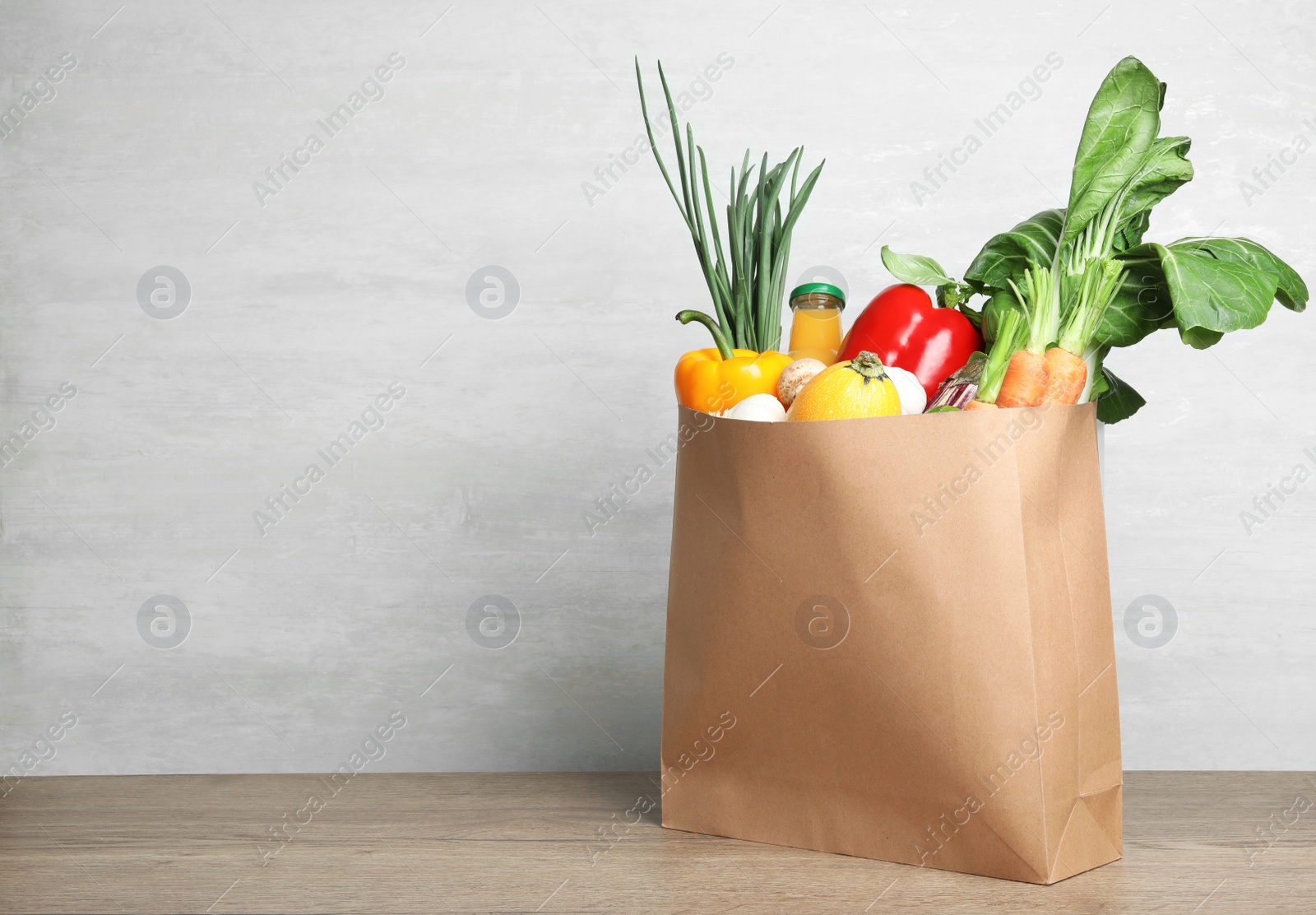 Photo of Paper bag with vegetables and bottle of juice on table against grey background. Space for text