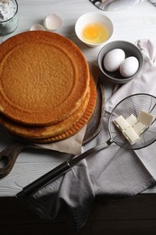 Photo of Delicious homemade sponge cake and ingredients on white wooden table, above view