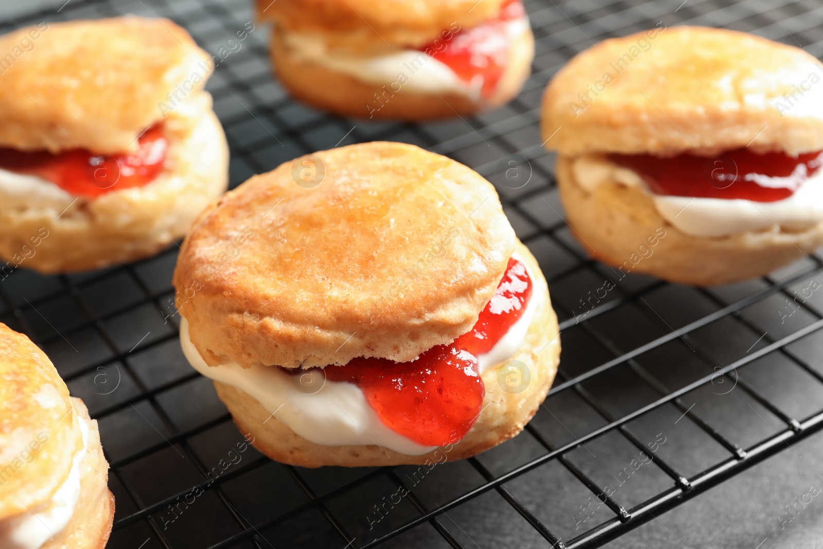 Photo of Tasty scones with clotted cream and jam on cooling rack, closeup