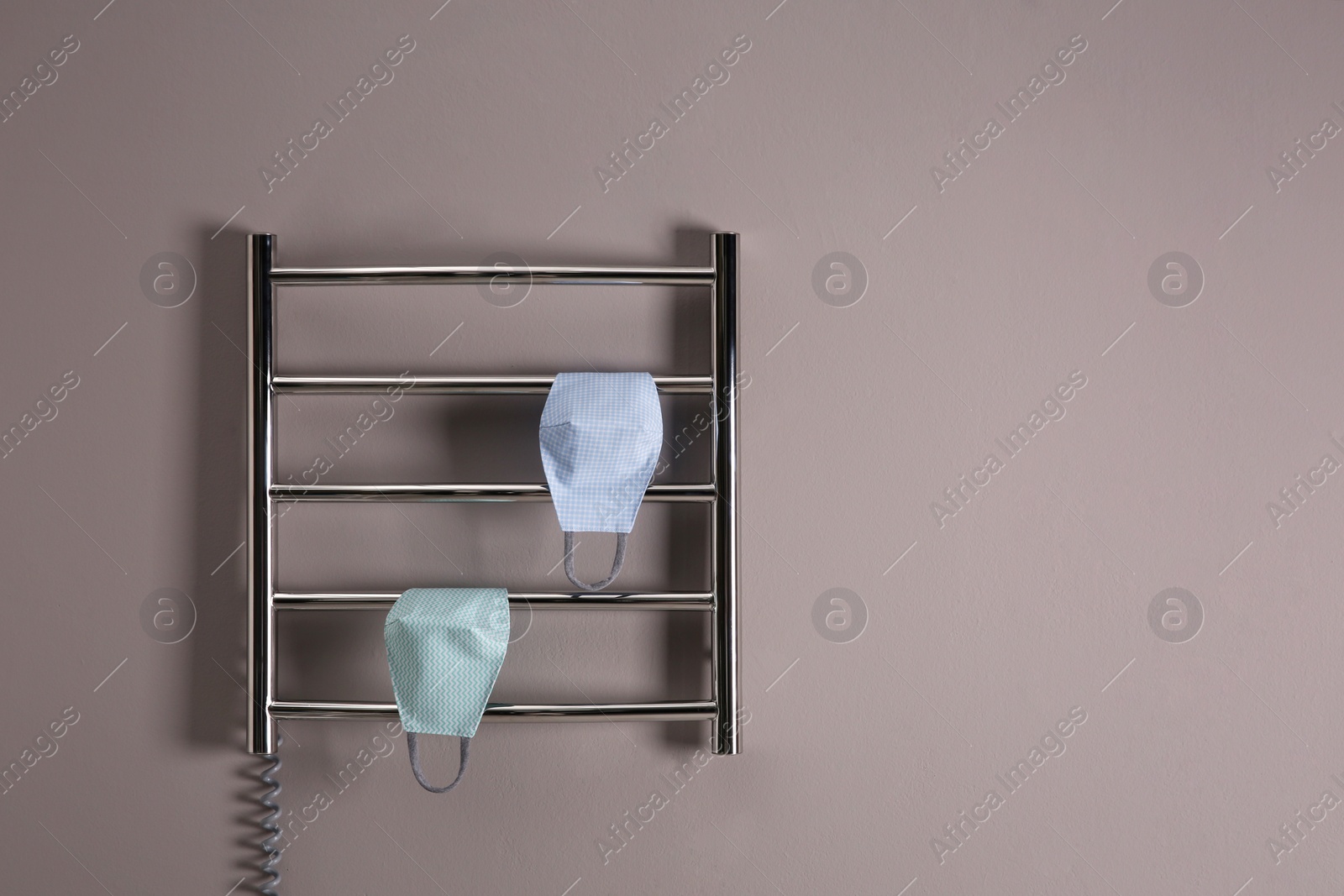 Photo of Modern heated towel rail with cloth face masks on grey wall. Space for text