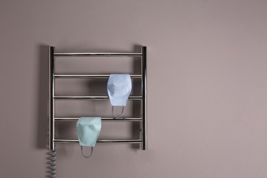 Photo of Modern heated towel rail with cloth face masks on grey wall. Space for text