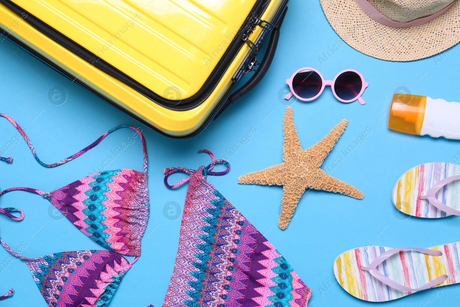 Photo of Yellow suitcase and beach objects on blue background, flat lay