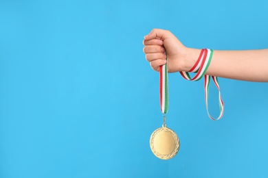 Woman holding gold medal on light blue background, closeup. Space for text