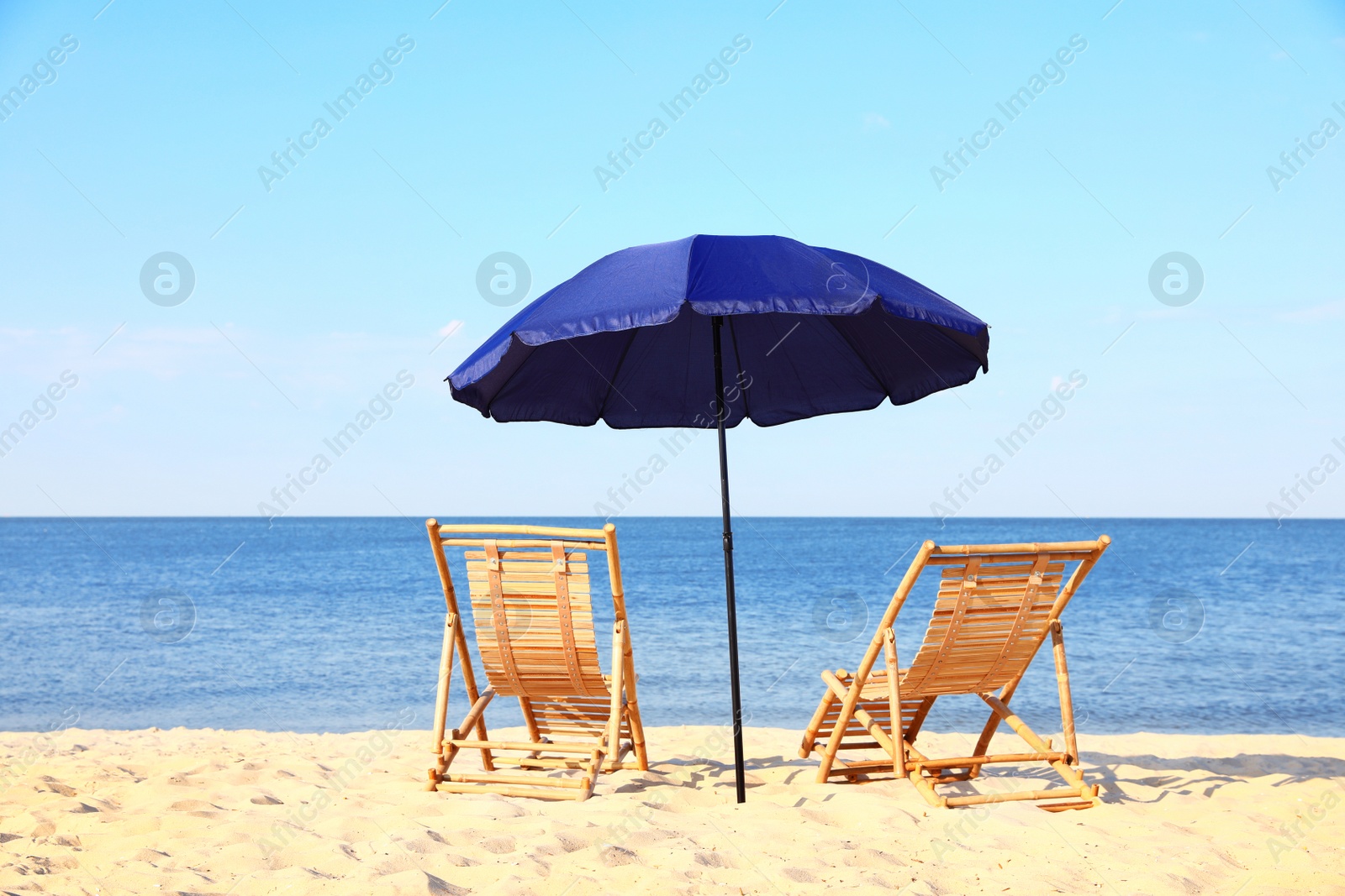 Photo of Empty wooden sunbeds and umbrella on sandy shore. Beach accessories