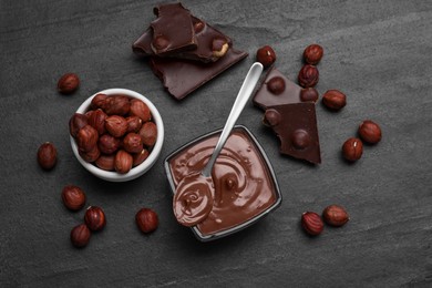 Bowl with tasty paste, chocolate pieces and nuts on black table, flat lay