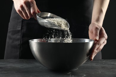 Photo of Making bread. Woman putting flour into bowl at grey textured table, closeup