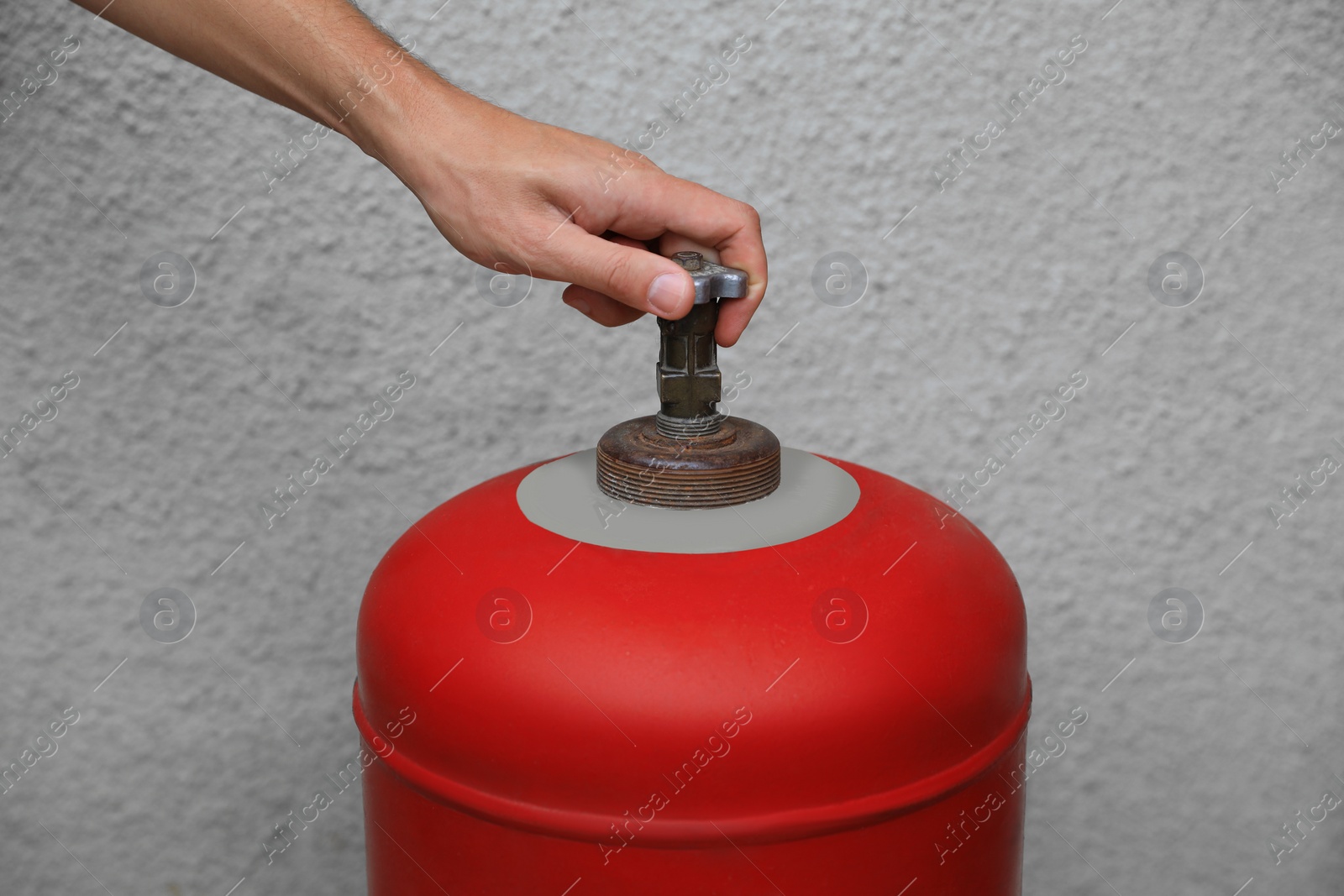 Photo of Man opening red gas cylinder near wall, closeup