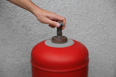 Photo of Man opening red gas cylinder near wall, closeup