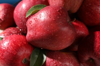 Photo of Ripe red apples with water drops and green leaves as background, closeup