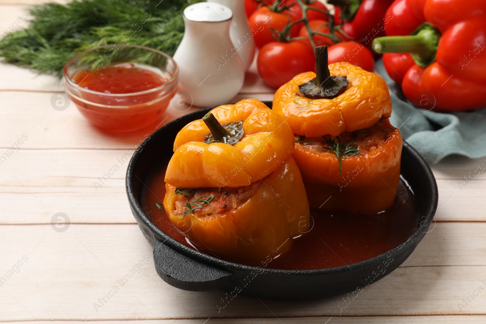 Photo of Tasty stuffed peppers in pan, sauce and products on light wooden table, closeup