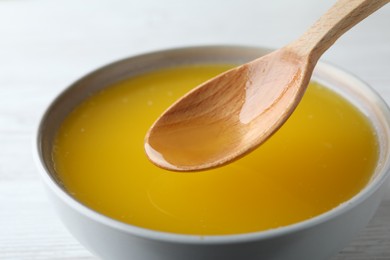 Photo of Spoon of clarified butter over bowl on white table, closeup