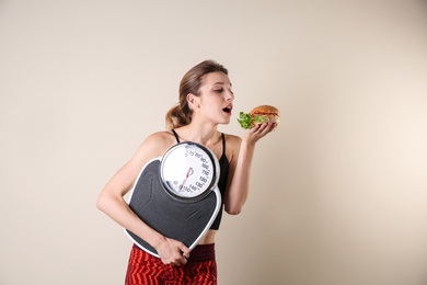 Photo of Young beautiful woman with scales and sandwich on light background. Weight loss motivation