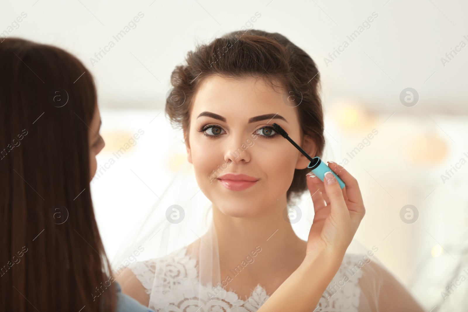 Photo of Makeup artist preparing bride before her wedding in room