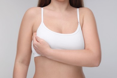 Photo of Mammology. Woman doing breast self-examination on light grey background, closeup