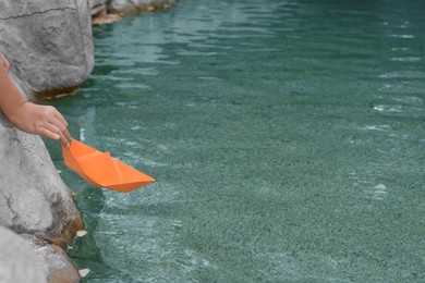 Kid launching small orange paper boat on water outdoors, closeup. Space for text