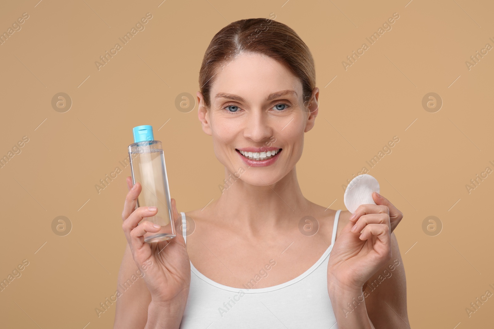 Photo of Beautiful woman with makeup remover and cotton pad on beige background
