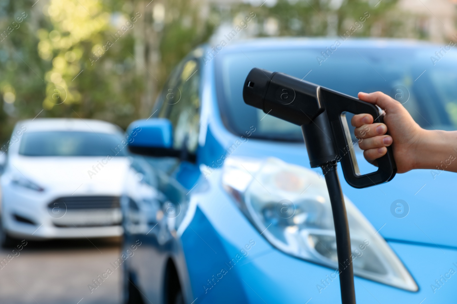 Photo of Woman holding power supply cable at electric vehicle charging station, closeup