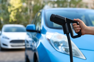 Woman holding power supply cable at electric vehicle charging station, closeup