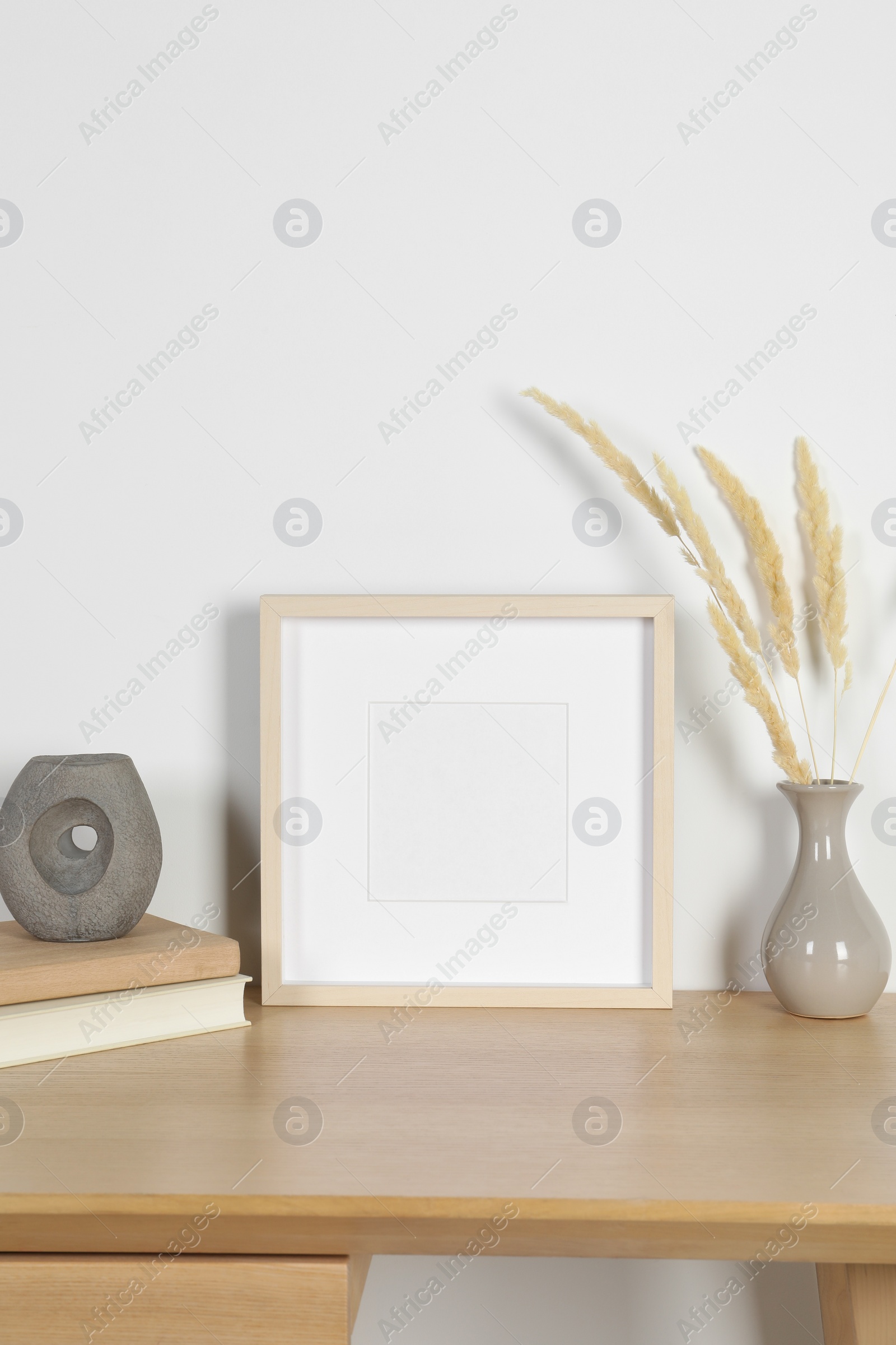 Photo of Empty photo frame and vase with dry decorative spikes on wooden table. Mockup for design