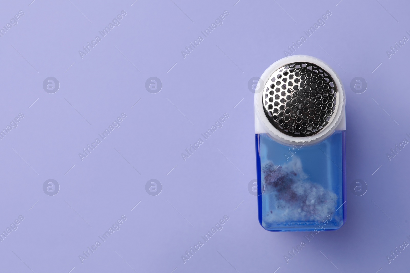 Photo of Fabric shaver with fuzz on lilac background, top view. Space for text