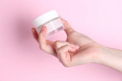 Woman holding jar of cream on pink background, closeup