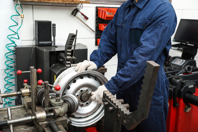 Photo of Man working with car disk lathe machine at tire service, closeup