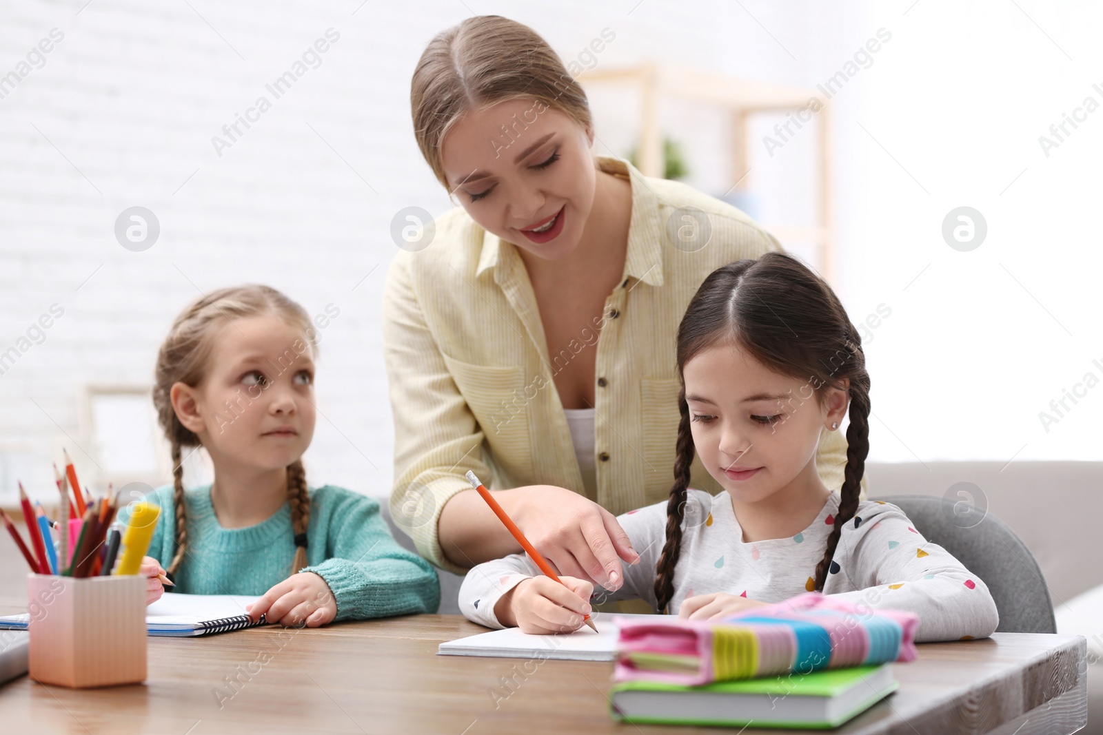 Photo of Mother helping her daughters with homework at table indoors