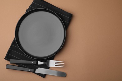 Photo of Clean plate with cutlery and napkin on light brown background, flat lay. Space for text