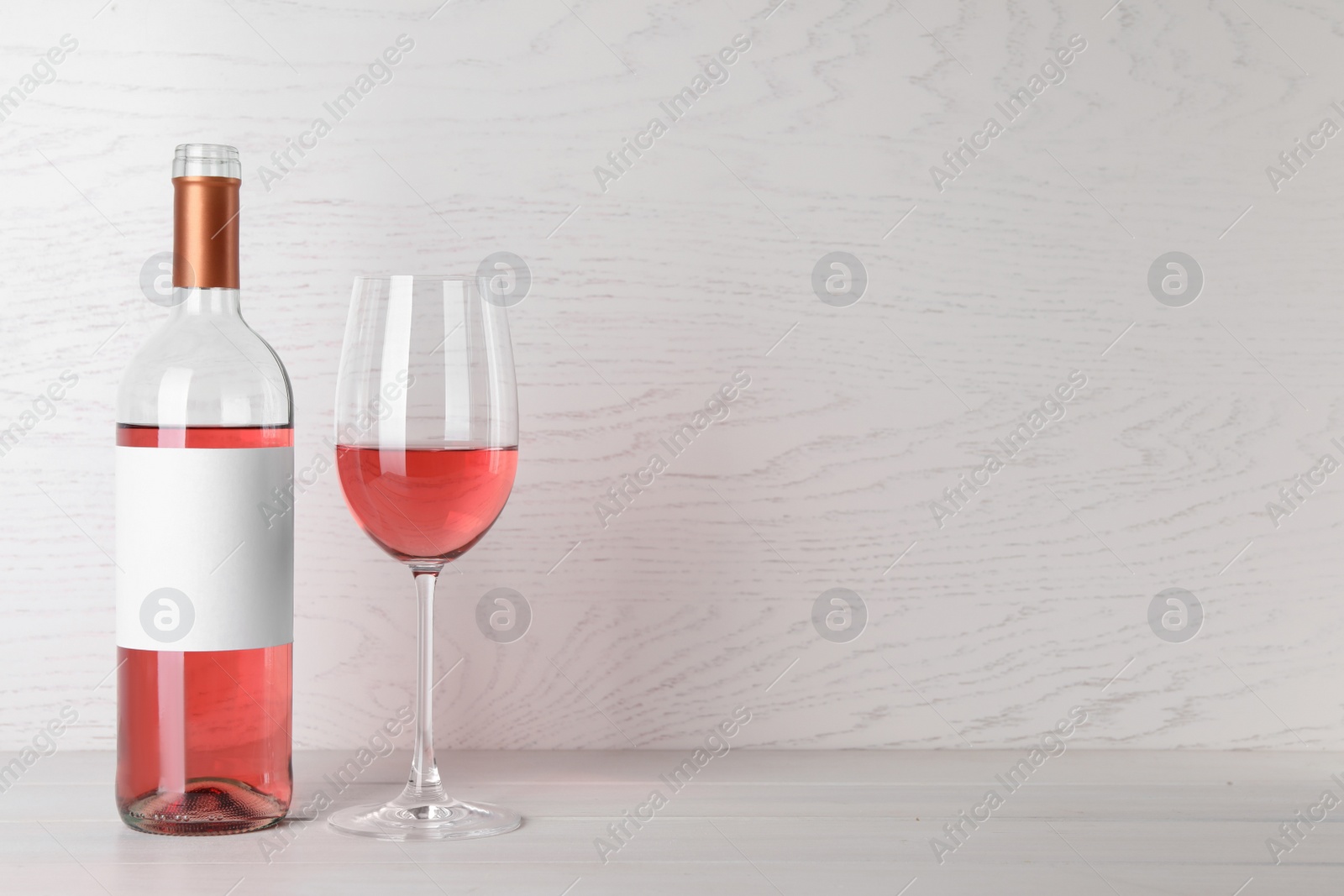 Photo of Bottle and glass of delicious rose wine on table against white wooden background. Space for text