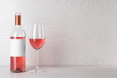 Bottle and glass of delicious rose wine on table against white wooden background. Space for text