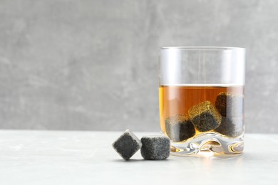 Photo of Whiskey stones and drink in glass on light marble table. Space for text