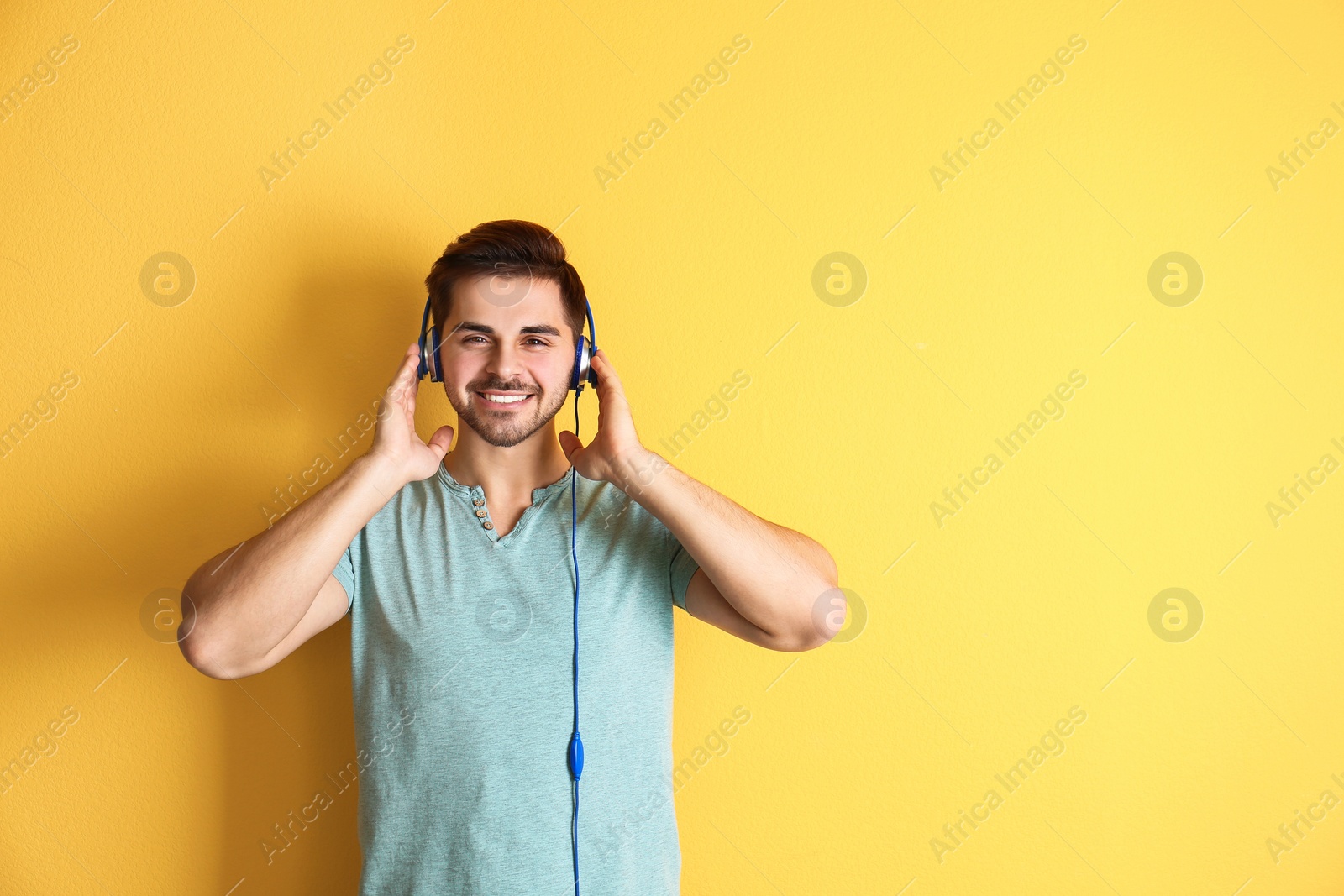 Photo of Handsome man with headphones enjoying music on color background. Space for text