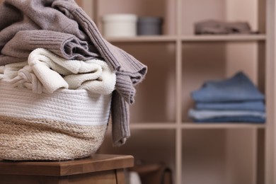 Photo of Wicker laundry basket overfilled with clothes on wooden stool indoors, closeup. Space for text