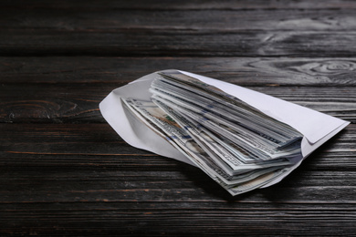 Photo of Envelope with dollar bills on black wooden table. Bribe concept