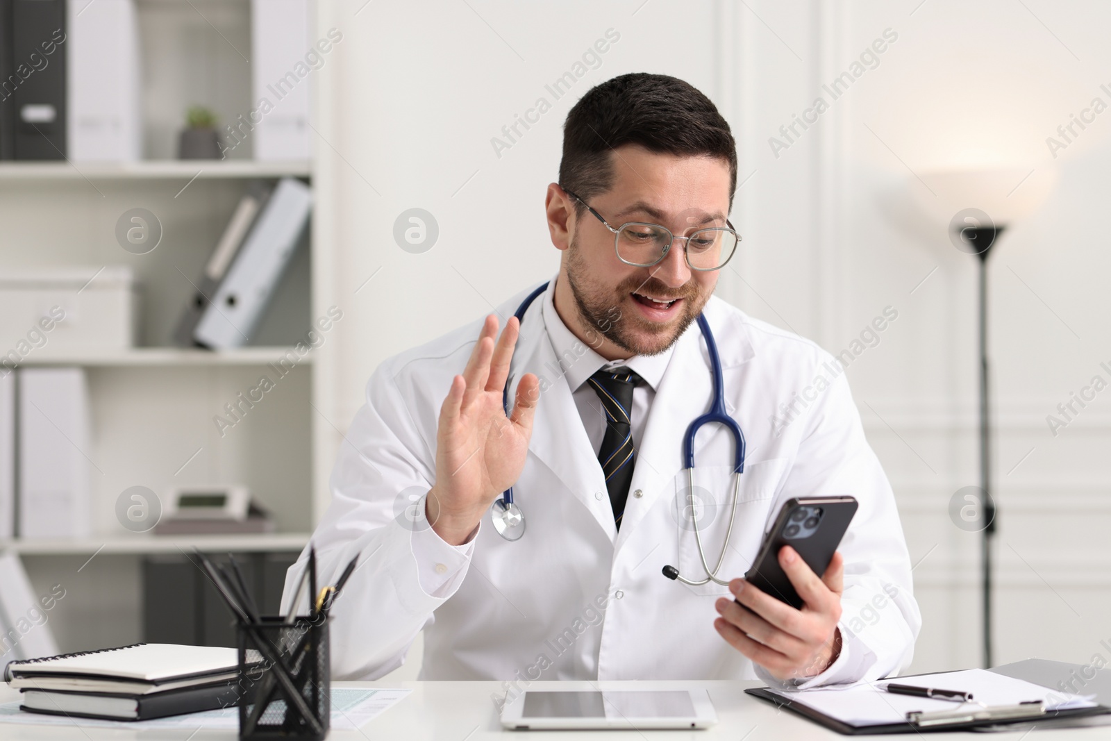 Photo of Doctor having online consultation via smartphone at table in clinic