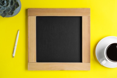 Photo of Clean small chalkboard, coffee, pen and plant on yellow background, flat lay