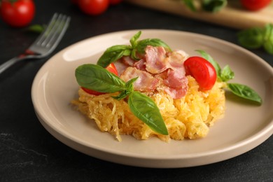 Photo of Tasty spaghetti squash with bacon and basil served on black table, closeup