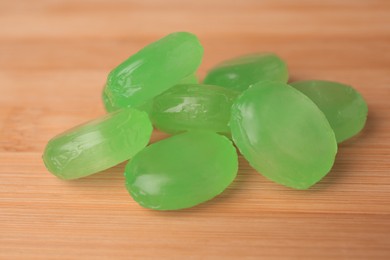 Photo of Many light green cough drops on wooden table, closeup