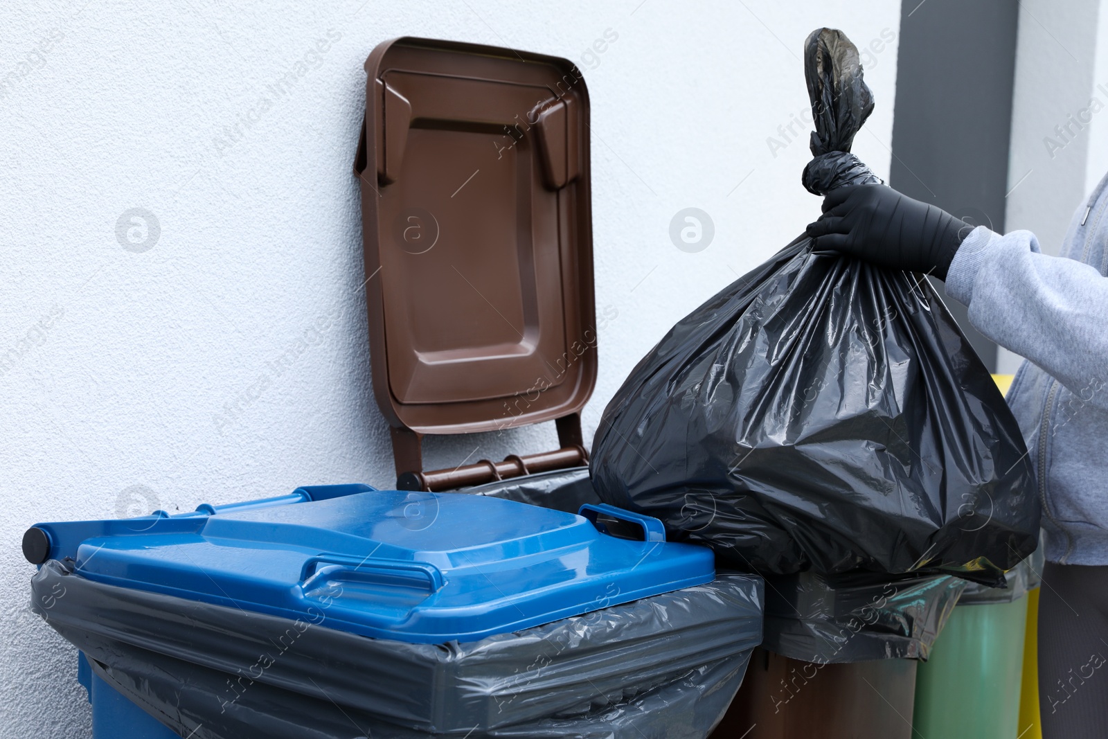 Photo of Woman throwing trash bag full of garbage in bin outdoors, closeup. Recycling concept