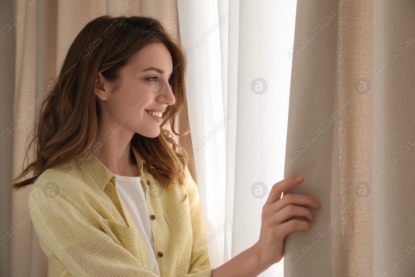 Photo of Woman opening window curtains at home in morning