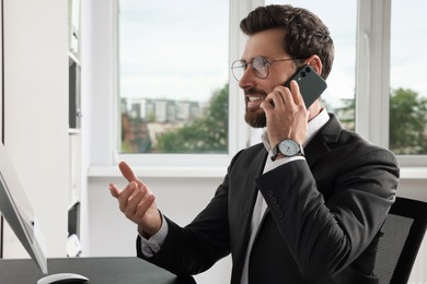 Photo of Handsome businessman talking on smartphone at workplace in office