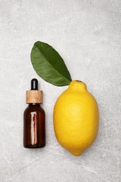 Photo of Bottle of essential oil with lemon and leaf on grey table, flat lay