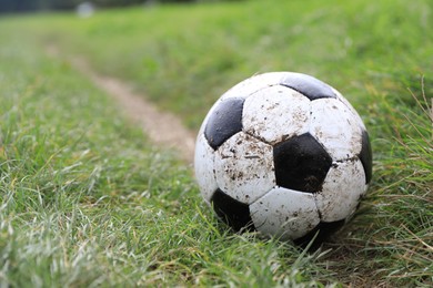 Dirty soccer ball on green grass outdoors, space for text